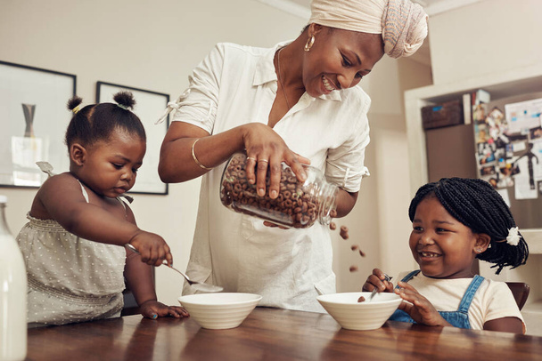 朝食の時間だ。Cropped shot of a young mother preparing cereal for her two adorable young daughters at home. - 写真・画像
