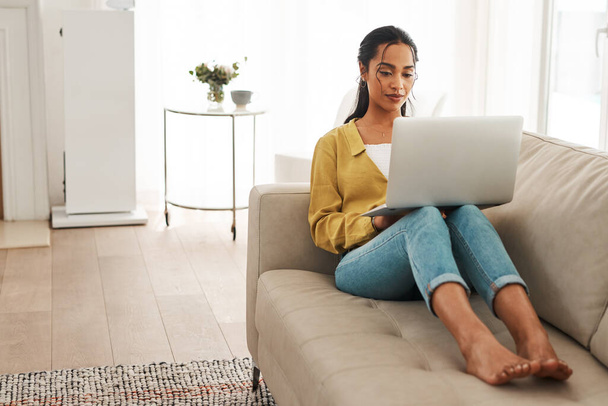 Getting through the day one task at a time. Full length shot of an attractive young businesswoman sitting on her couch and blogging from her laptop while at home. - Foto, Imagen