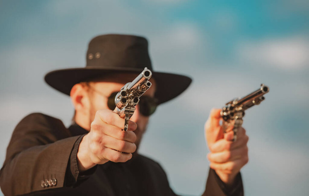 Sheriff in black suit and cowboy hat shooting gun, close up western portrait. Wild west, western, man with vintage pistol revolver and marshal ammunition. - Foto, Imagem
