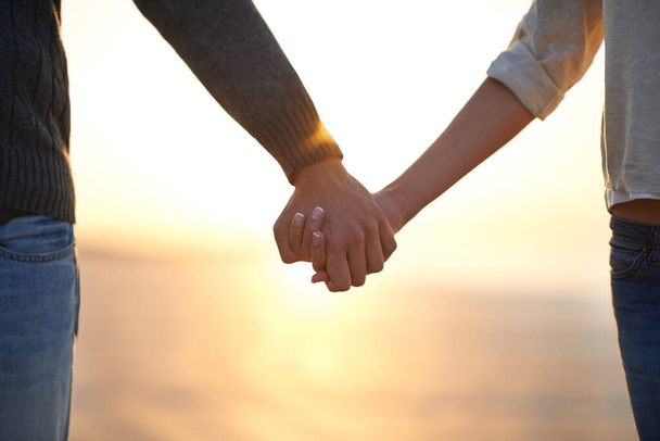 Mostrando su compromiso con la relación. Cultivado whot de una joven pareja cogida de la mano en la playa. - Foto, imagen