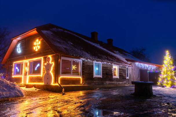 Paisaje nocturno con un patio de Navidad decorado, decoraciones ligeras, reflejos de luz de colores en un camino húmedo en primer plano - Foto, Imagen