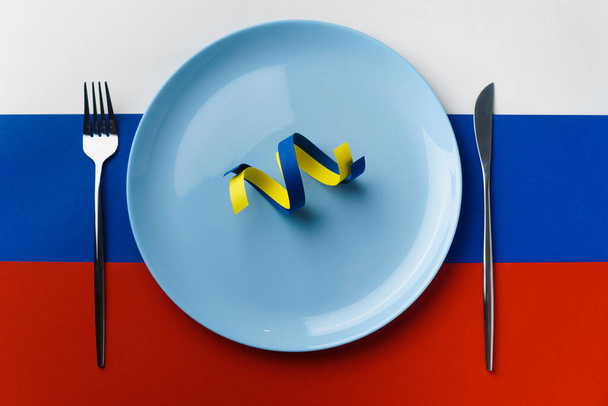 Cintas azules y amarillas como símbolo de Ucrania en el plato de la bandera de Rusia. Rusia quiere comer Ucrania - Foto, Imagen