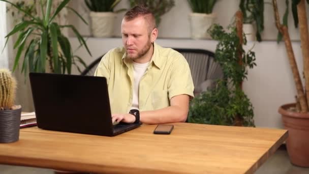 Freelancer hombre que trabaja con el ordenador portátil en la mesa en casa, mecanografía masculina en el ordenador para el trabajo remoto - Metraje, vídeo
