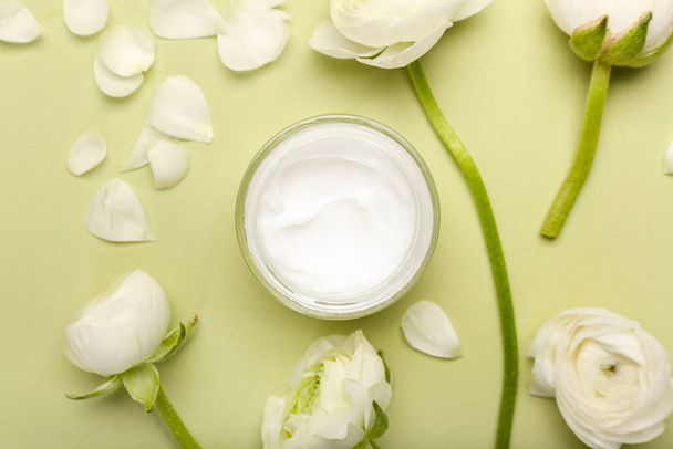 Összetétel egy üveg kozmetikai termékkel és ranunculus virágokkal zöld alapon - Fotó, kép