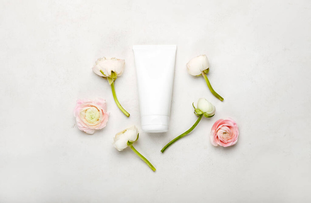 Tube of cosmetic products and beautiful ranunculus flowers on light background - Fotoğraf, Görsel