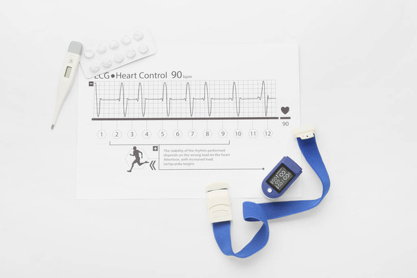 Composición con oxímetro de pulso, cardiograma y termómetro sobre fondo blanco - Foto, imagen