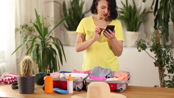 Travel woman packing suitcase, check things on the smartphone, getting ready for summer vacation trip preparing luggage for holidays. - Footage, Video