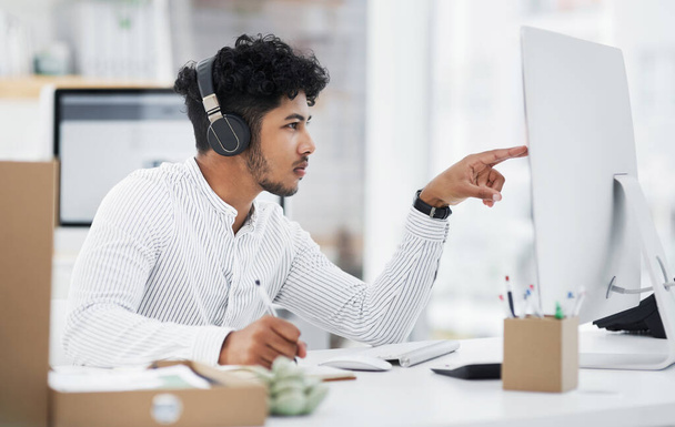 Raději si to pečlivě pročtu. Snímek mladého podnikatele ve sluchátkách při práci na počítači v kanceláři. - Fotografie, Obrázek