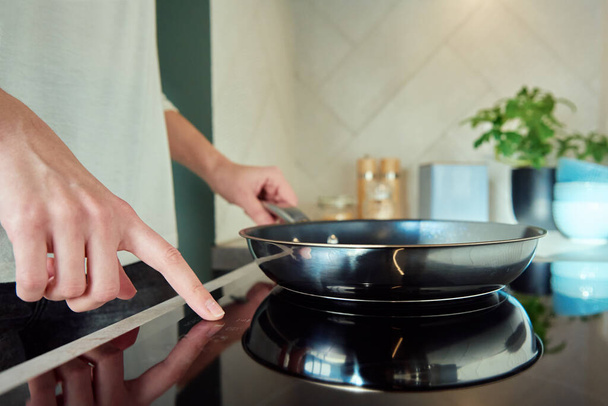 Σύγχρονη συσκευή κουζίνας, Γυναίκα χέρι ενεργοποιήσετε επαγωγική σόμπα με τηγάνι χάλυβα, δάχτυλο αγγίζοντας το κουμπί αισθητήρα στην επαγωγή ή ηλεκτρικές εστίες - Φωτογραφία, εικόνα