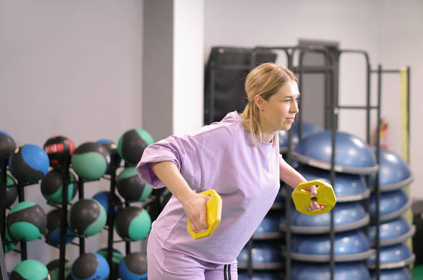 Woman holding a lightweight disks for working out arms and triceps in gym. Exercising and workout for weight loss and losing body fat - Foto, imagen