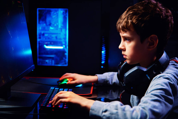 Teenager boy play computer video game in dark room, use neon colored rgb mechanical keyboard, workplace for cybersport gaming, children gaming addiction - Фото, изображение