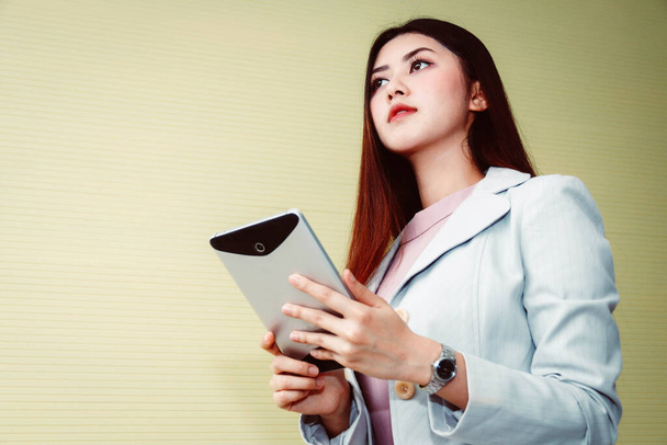 Портативна азіатська бізнес-жінка використовує ноутбук у випадковому офісному приміщенні, дивлячись на зовні. - Фото, зображення