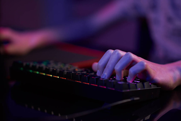 Professzionális játékos játszani számítógépes videojáték sötét szobában, használja neon színű rgb mechanikus billentyűzet, hely cybersport játék - Fotó, kép