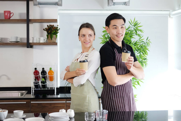 Uśmiechnięty azjatycki barista młody mężczyzna i biała kelnerka serwująca dwie szklanki gorącej kawy i zabierająca do domu dla klientów w barze w kawiarni. Rozpoczęcie działalności gospodarczej Concept - Zdjęcie, obraz