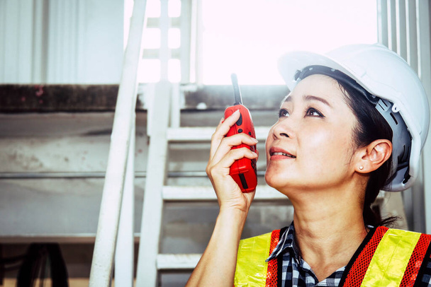 Retrato de una hermosa mujer ingeniero capataz que trabaja en el campo en un sitio de construcción utilizando radios walkie talkie para dirigir tareas para mejorar el trabajo en equipo. - Foto, imagen