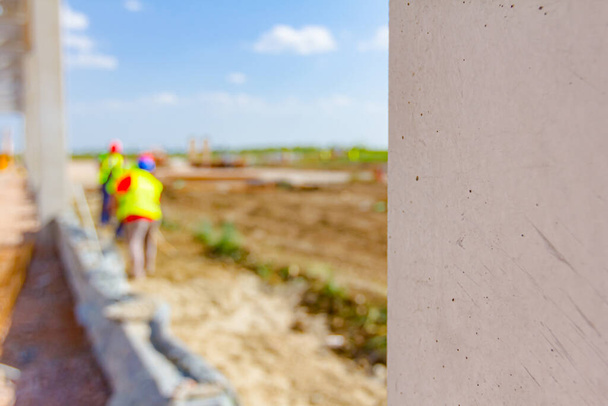 Clouse-up zicht op balk, pilaar van onafgewerkt beton. Mensen werken op de achtergrond met veiligheidsvesten en helmen. - Foto, afbeelding
