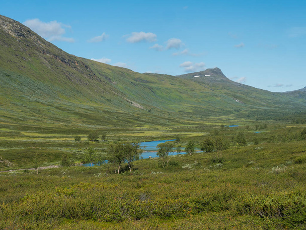 Увлекательный северный пейзаж, тундра в шведском местечке с голубой арктической рекой и озером, зеленые холмы и горы на пешеходной тропе Паджелантфеден. Летний день, голубое небо, белые облака - Фото, изображение
