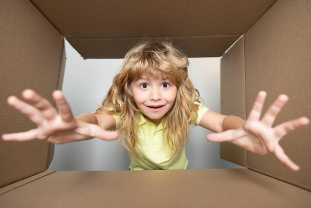 Funny child boy is opening gift and looking inside cardboard box. Child with open box take by hand gift. - Foto, imagen