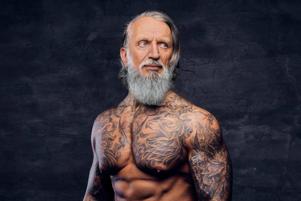 Muskulöser älterer Mann mit tätowiertem Körper vor dunklem Hintergrund - Foto, Bild