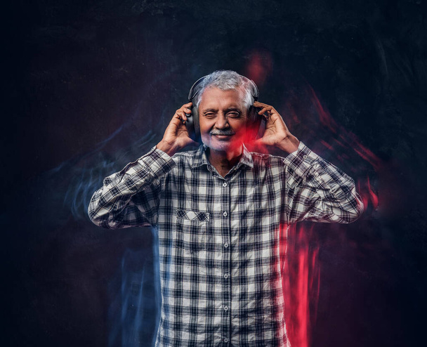 Cheerful old man with headphones dressed in plaid shirt - Foto, afbeelding