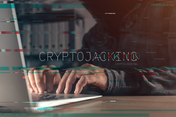 Cryptojacking concept with faceless hooded hacker working on laptop computer, with glitch effect and selective focus - Φωτογραφία, εικόνα
