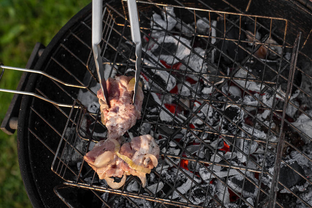 Closeup photo of grill tongs holding seasoned pork. Grilling meat outside on a barbecue grill. Outdoor grill party in the summer season. Healthy barbecue.  - Photo, Image