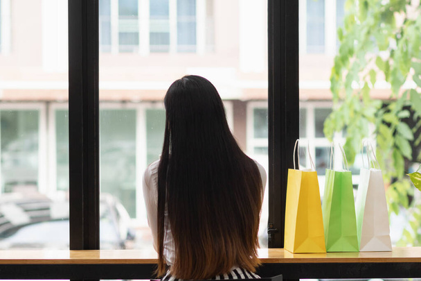 Nuori nainen laittaa monivärisen paperipussin tiskille ostoksen jälkeen ostoskeskuksessa ja haluaa rentoutua ja tarkistaa tuotteet, joita hän on ostanut iloisesti.. - Valokuva, kuva
