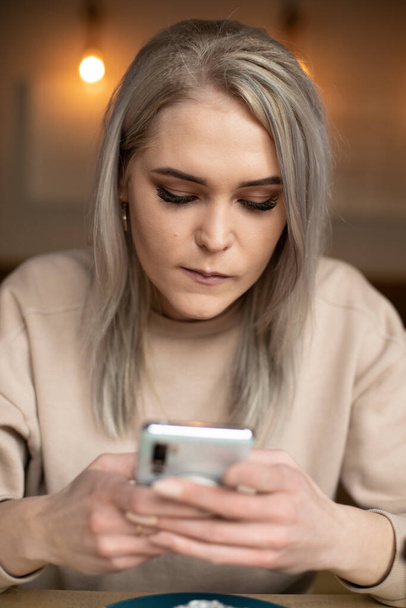 Verticale foto van doordachte geconcentreerde blonde vrouw met make-up, typen en surfen internet technologie, smartphone - Foto, afbeelding