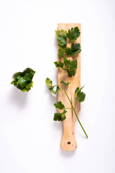 heart-shaped bowl with parsley leaves, near cutting board with parsley sprigs on top. White background. love concept for parsley. aromatic herb. - Photo, Image