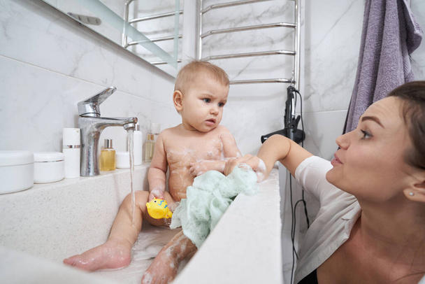 Baby with bath toy in hand spending time in bathroom during the hygiene procedure - Foto, Bild