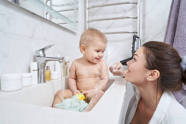 Cute little kid in bathroom sink washing in water from valve - Foto, Bild