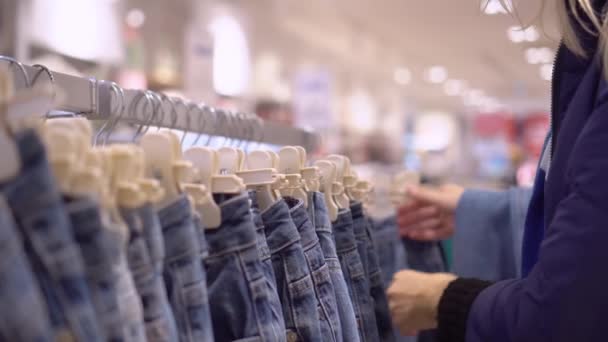 mãos de mulher jovem escolher jeans que penduram no cabide na loja de roupas. - Filmagem, Vídeo