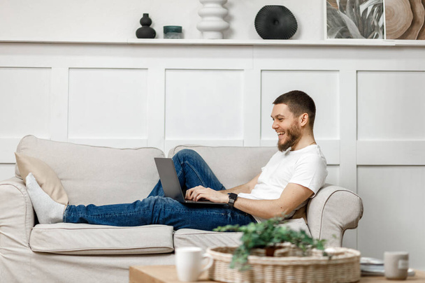 молодий чоловік вдома на дивані з ноутбуком
 - Фото, зображення