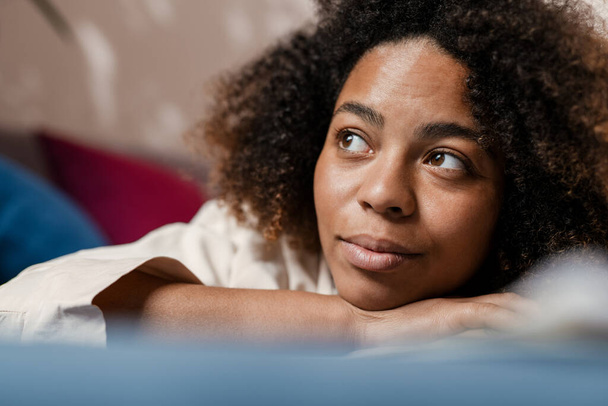 Mladá černošky žena dívá stranou, zatímco leží doma - Fotografie, Obrázek