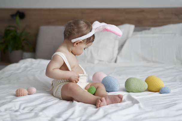 Tavşan kostümlü şirin beyaz kız evde yatakta oturuyor.  - Fotoğraf, Görsel