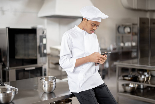 Latin chef with phone in professional restaurant kitchen - Photo, Image