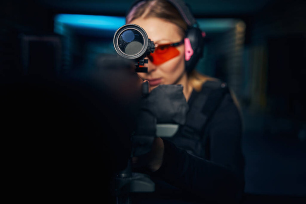 Εστιασμένη νεαρή γυναίκα πυροβολεί ένα σύγχρονο πυροβόλο όπλο - Φωτογραφία, εικόνα