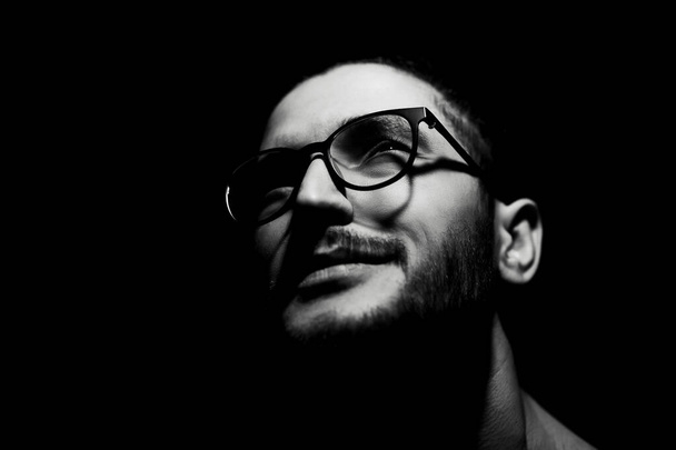 Schwarz-weißes, nahes dunkles Porträt eines jungen lächelnden Mannes mit Brille. - Foto, Bild
