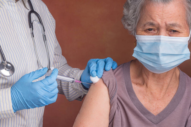 Ο γιατρός κάνει εμβολιασμό σε μια ηλικιωμένη γυναίκα. Προστασία από ιούς. Έννοια των ηλικιωμένων και της υγειονομικής περίθαλψης. - Φωτογραφία, εικόνα