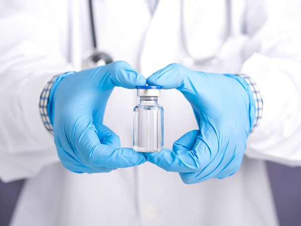 Az orvos egy vakcinás üveget mutat szürke háttérrel. Védőoltás és vírusfertőzés elleni kezelés. Egy közeli kép. Az orvosi koncepció és a vírus elleni küzdelem. - Fotó, kép