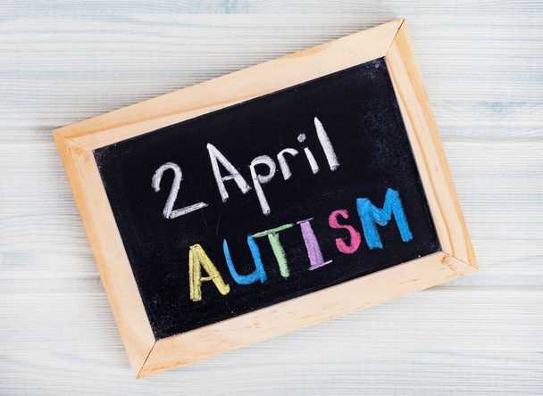 Слово Аутизм, написане вручну на дошці з блакитними шматочками головоломки
 - Фото, зображення