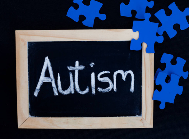 Słowo Autyzm odręcznie napisane na tablicy z kawałkami niebieskich łamigłówek - Zdjęcie, obraz