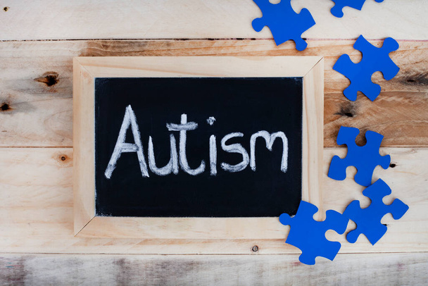 Le mot Autisme écrit à la main sur un tableau avec des pièces de puzzle bleu - Photo, image