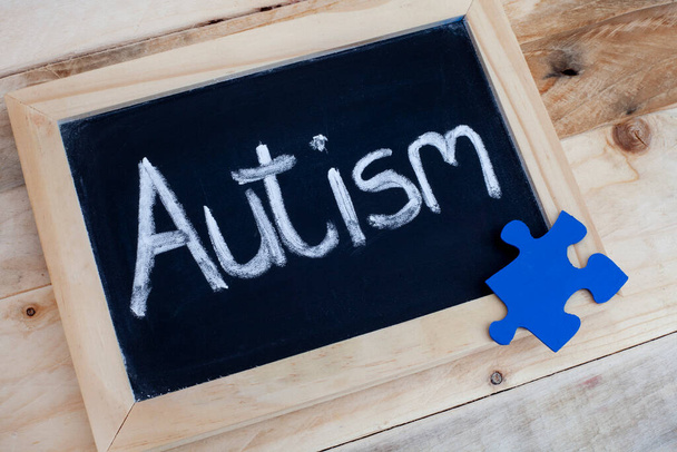 La palabra autismo escrito a mano en pizarra con piezas de rompecabezas azul - Foto, imagen