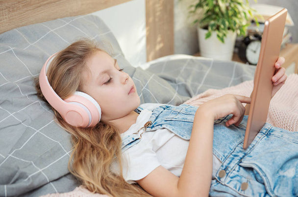 Cute little girl in headphones is using a tablet  at home - Foto, Imagen