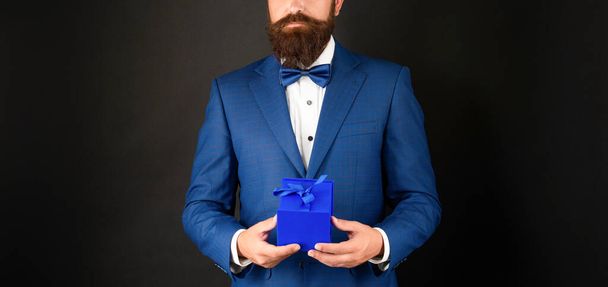 cropped man in tuxedo bow tie formalwear on black background with gift box. boxing day - Zdjęcie, obraz