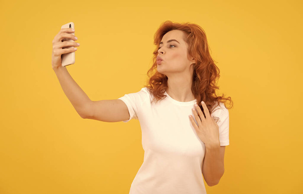 Frau pustet Luftkuss Selfie mit Kamera Handy gelben Hintergrund, Selbstporträt-Foto - Foto, Bild