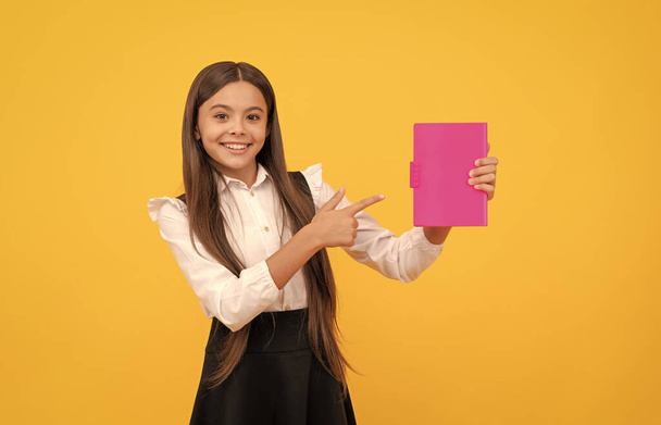 счастливая девочка-подросток в школьной форме указывает пальцем на книгу, рекламу - Фото, изображение