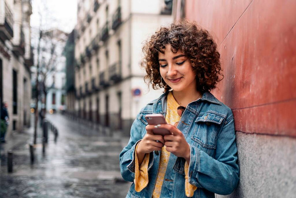 Молода жінка використовує телефон на вулиці
 - Фото, зображення