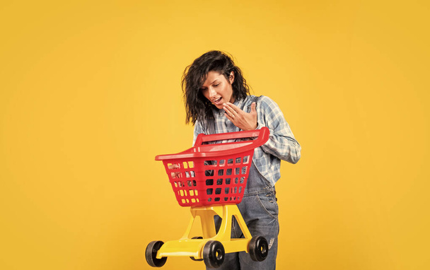 cheerful lady in shirt denim style carry shopping trolley on yellow background, shopping - Foto, Imagem